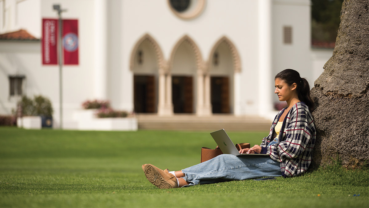 LMU student works under a tree in Sunken Garden